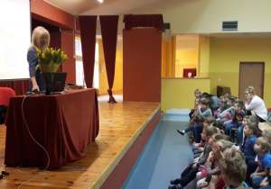 Pani Sędzia stoi za biurkiem na scenie, przedszkolaki siedzą na widowni