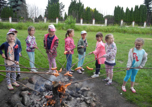 Dziewięć dziewczynek piecze kiełbaski na patykach nad ogniskiem