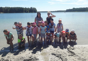 Zdjęcie grupowe Jabłuszek na tle jeziora, dzieci wraz z dwoma Paniami stoją po kostki w wodzie