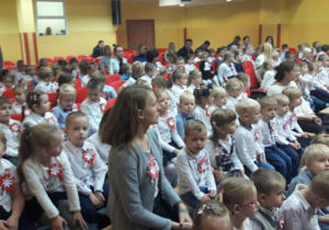 Przedszkolaki czekają na występy kolegów, dzieci są ubrane na galowo, mają przyczepione do koszulek kotyliony