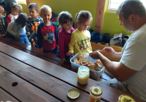 Dzieci stoją w kolejce po chlebek z miodem, Pan Pszczelarz smaruje chlebki miodkiem