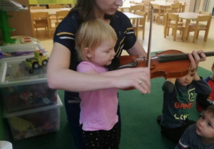 Dziewczynka gra na skrzypcach, Pani jej pomaga w trzymaniu instrumentu