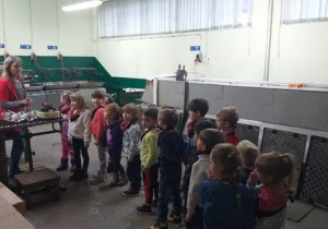 Dzieci podczas zwiedzania fabryki, słuchają Pani stojącej obok maszyny