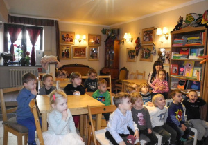 Dzieci z grupy Koty w Baśniowej Kawiarence, siedzą przy stolikach, patrzą na scenę