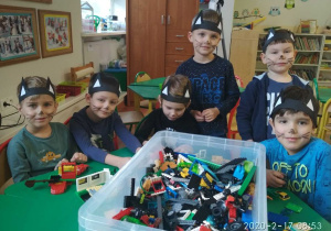 Chłopcy w przebraniach kotów, siedzą przy stoliku, na stole pudełko z klockami lego
