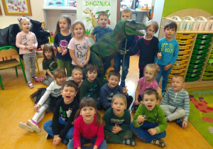 Zdjęcie grupowe z dinozaurem na tle plakatu: Dzień dinozaura