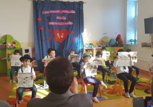 Sowy podczas tańca Va bank, siedzą na krzesłach z gazetami, w tle napis: Cała nasza gromadka kocha babcię i dziadka