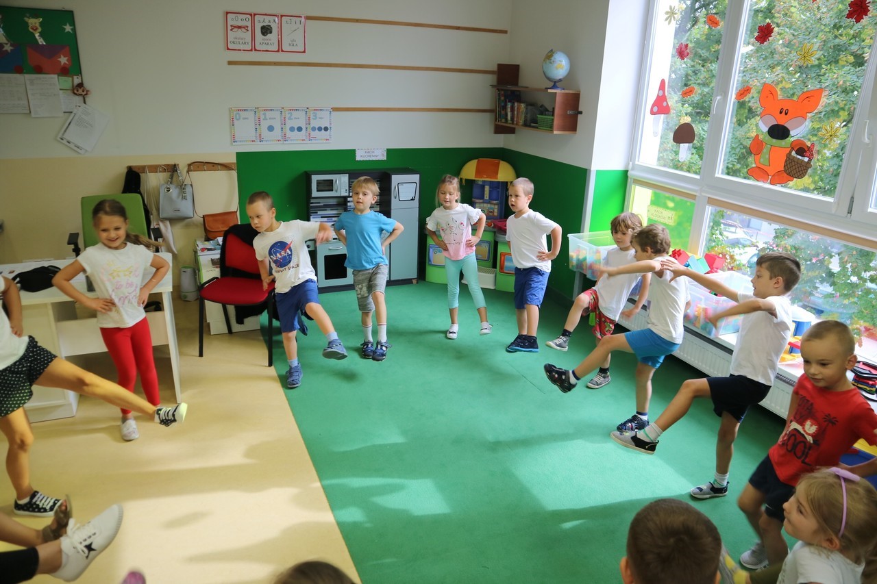 Dzieci z grupy Małpki podczas wykonywania ćwiczeń gimnastycznych, przedszkolaki stoją na jednej nodze, próbuja utrzymać równowagę