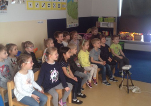Dzieci podczas warsztatów, siedza na krzesłach, słuchają prowadzących warsztaty