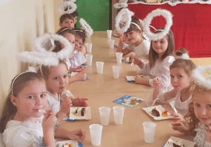 Dzieci z grupy Jabłuszka siedzą przy stołach, jedzą ciasto