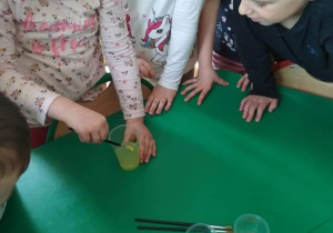 Dziewczynka miesza żółtą farbę w plastikowym kubku z wodą