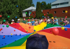Dzieci z chustą animacyjną, na której są gumowe, kolorowe piłki