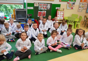 Dzieci w strojach laboranta siedzą na dywanie