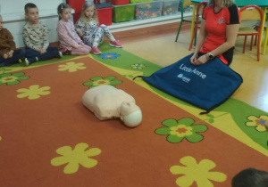 Pani ratownik przed nią fantom, dookoła siedzą dzieci