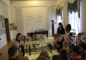 Dzieci oglądaja eksponaty muzeum w szkalnych gablotach