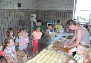 Dzieci podczas warsztatów, patrzą jak pani zwija makowiec