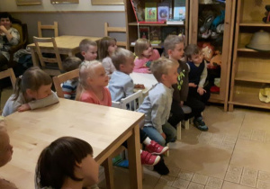 Dzieci podczas przedstawienia, siedzą przy stolikach, patrzą na scenę