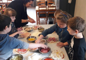 Dzieci podczas nakładania dodatków na swoje małe pizze