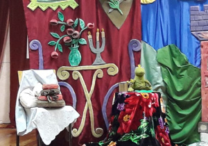 Żabka gotowa do spożywania posiłku siedzi na krześle, na drugim krześle leży tort