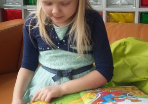 Dziewczynka na pomarańczowej kanapie ogląda ilustracje w książce