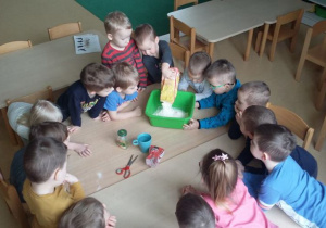 Dzieci siedzą przy stoliku, jedno z nich wspypuje mąkę do miski