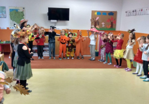 Dzieci podczas zabawy, stoja w półkolu, powtarzają ruchy po nauczycielce