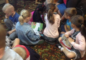 Dzieci oglądają książki na dywanie wraz z panią z biblioteki