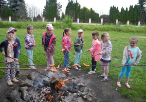 Dziewięć dziewczynek piecze kiełbaski na patykach nad ogniskiem