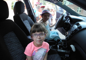 Dwie dziewczynki siedzą w radiowozie, na miejsscu kierowcy oraz na miejscu obok kierowcy