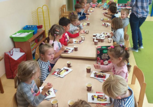 Dzieci z grupy Jabłuszka w sali, siedzą przy stolikach, jedzą słodki poczęstunek