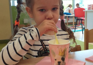 Dziewczynka pije sok z kubeczka przez słomkę