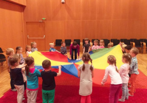 Dzieci stoją z chustą animacyjną na dywanie