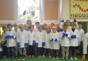 Dzieci w strojach naukowców - fartuchy, okulary, rękawiczki - wraz z prowadzącymi warsztat
