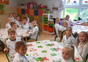 Dzieci podczas warsztatów, siedzą przy stolikach czekają na doświadczenia