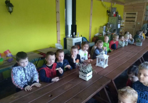 Dzieci jedzą chlebek z miodem, siedzą przy drewnianych ławach