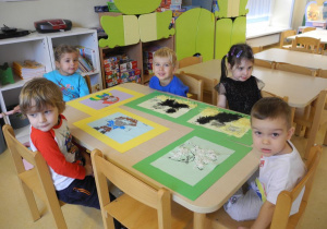 Dzieci po ukończeniu pracy plastycznej, siedzą przy stoliku, przed nimi prace plastyczne