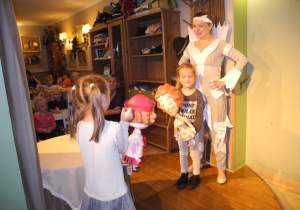 Dwie dziewczynki na scenie Baśniowej Kawiarenki z lalkami, obok aktorka Baśniowej Kawiarenki