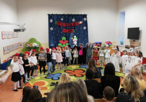 Impreza w Jabłuszkach, dzieci stoją w półkolu, są przebrane w stroje bohaterów scenariusza świątecznego (bałwanki, zwierzątka, na galowo), w tle napis: Wesołych Świąt