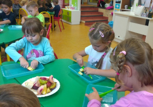 Przy stole siedzą trzy dziewczynki z grupy Sowy, kroją owoce na sałatkę