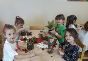Dziewczynki przy stoliku podczas wykonywania swojego lasu w słoiku, umieszczają w nim dary jesieni