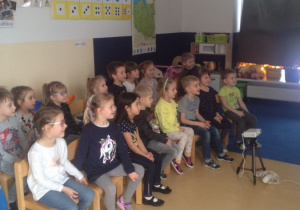 Dzieci podczas warsztatów, siedza na krzesłach, słuchają prowadzących warsztaty