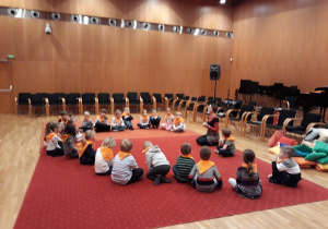 Dzieci podczas warsztatów, siadzą na dywanie słuchają Pani prowadzącej warsztat