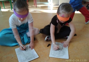 Dziewczynki podczas rysowania z zawiązanymi oczami według wskazówek nauczycielki