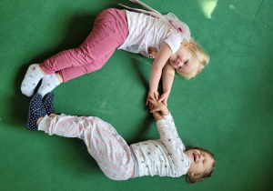 Dwie dziewczynki stworzyły kształt serca na dywanie łapiąc się za ręce i dotykając stopami