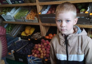 Chłopiec stoi na tle skrzynek z owocami