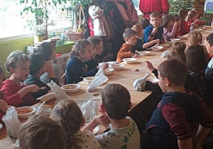 Dzieci przy stołach jedzą zupkę a Mikołaj przechadza się wokół nich