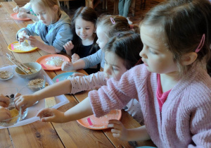 Dzieci podczas warsztatów, ozdabiają ciasto na bułkę ziarnami