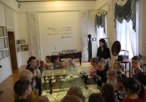 Dzieci oglądaja eksponaty muzeum w szkalnych gablotach