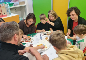 Rodzice wraz z dziećmi przy stole dekorują pierniki