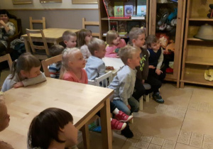 Dzieci podczas przedstawienia, siedzą przy stolikach, patrzą na scenę